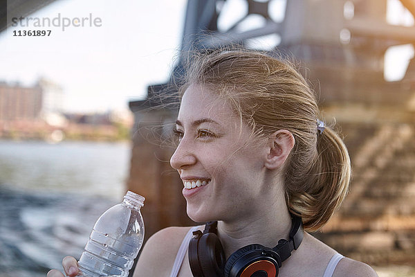 Junge Frau am Fluss  trägt Kopfhörer um den Hals  hält Wasserflasche  New York City  USA