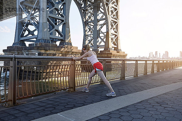 Junge Frau  die im Freien trainiert und sich unter der Williamsburg-Brücke erstreckt  New York City  USA