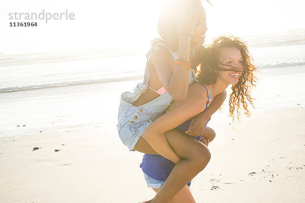 Junge Frau nimmt eine Freundin am Strand huckepack  Kapstadt  Südafrika
