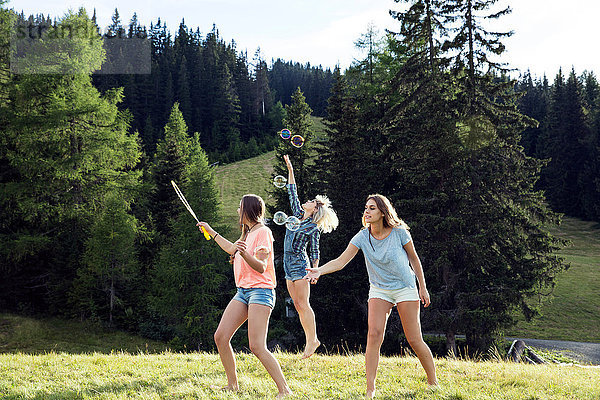 Drei erwachsene Freundinnen blasen und springen für Blasen im Feld  Sattelbergalm  Tirol  Österreich