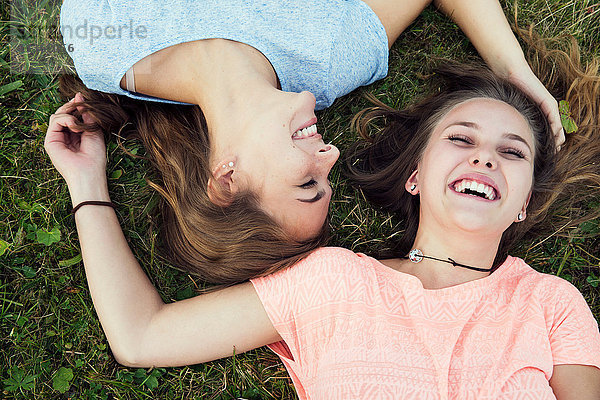 Portrait von zwei jungen Frauen  die im Gras liegen und lachen