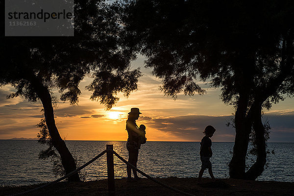 Silhouette von Mutter und Kindern am Wasser bei Sonnenuntergang  Italien