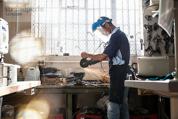 Junger Mann mit Winkelschleifer am Schraubstock in der Reparaturwerkstatt