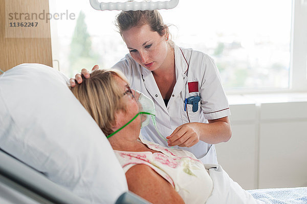 Krankenschwester  die den Patienten im Krankenhausbett mit Sauerstoffmaske pflegt