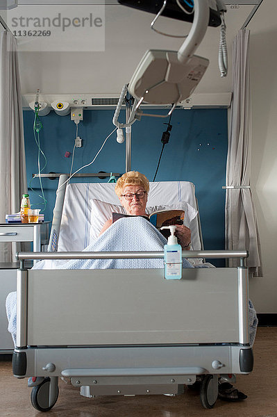 Patient im Krankenhausbett liest Zeitschrift