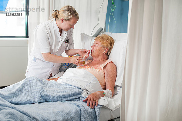 Krankenschwester hilft Patientin im Krankenhausbett beim Trinken
