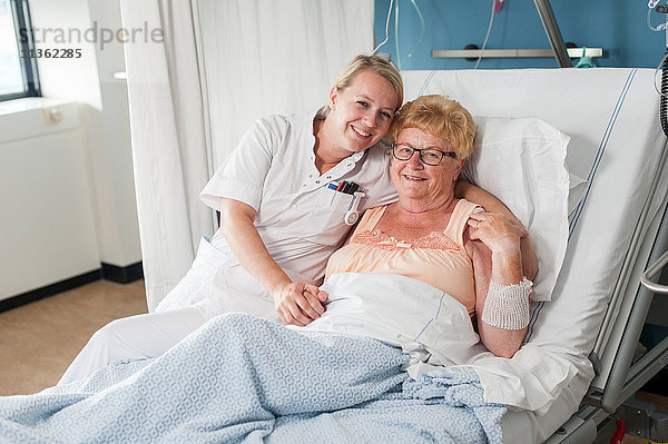 Krankenschwester und Patient auf Krankenhausbett  die lächelnd in die Kamera schauen