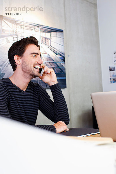 Mann im Büro benutzt Mobiltelefon und schaut lächelnd weg