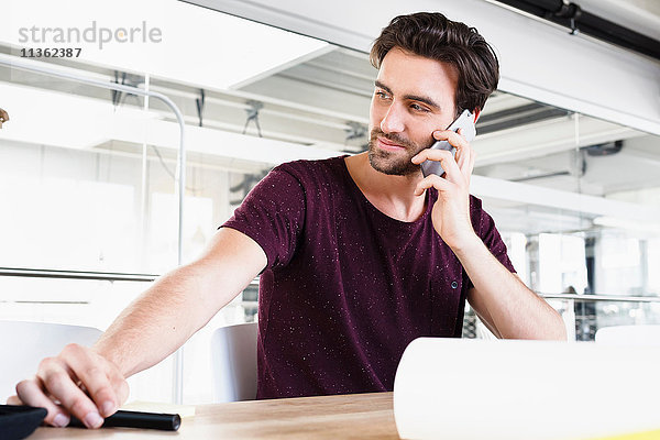 Mann im Büro mit Mobiltelefon  schaut weg