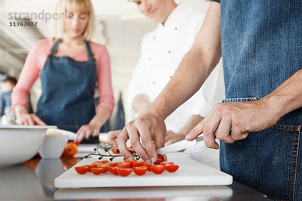 Koch und Ehepaar in der Küche schneiden Tomaten in Scheiben