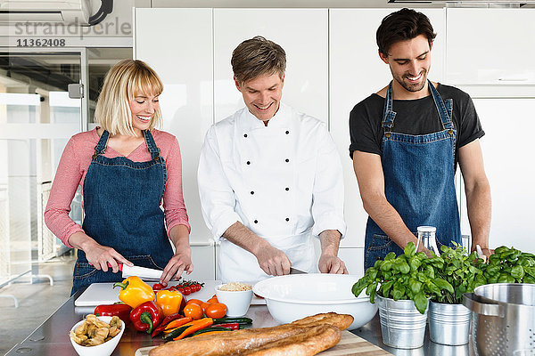 Koch und Ehepaar in der Küche beim Gemüseschneiden