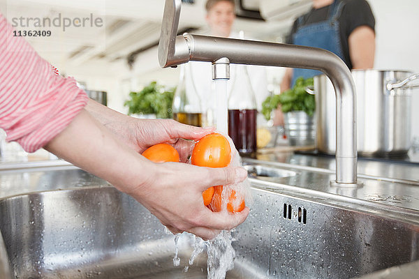 Schrägansicht der Hände einer Frau  die Tomaten unter dem Wasserhahn wäscht