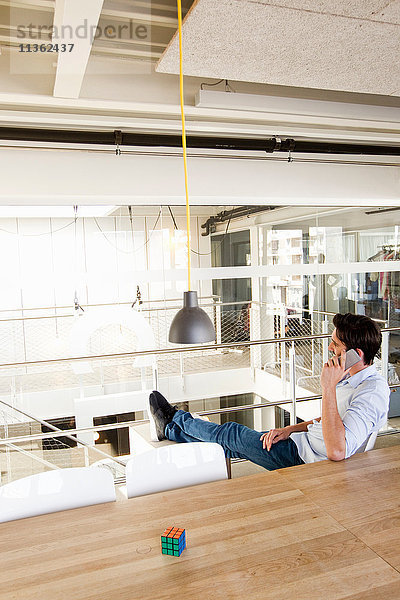 Mann im Büro  Beine hochgelagert  mit Mobiltelefon