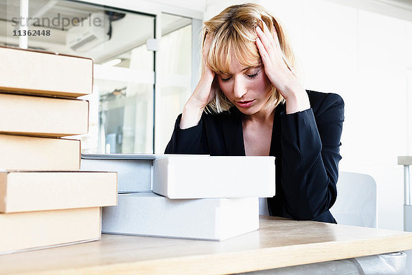 Geschäftsfrau mit einem Stapel Bücher  Kopf in Händen  die gestresst aussehen