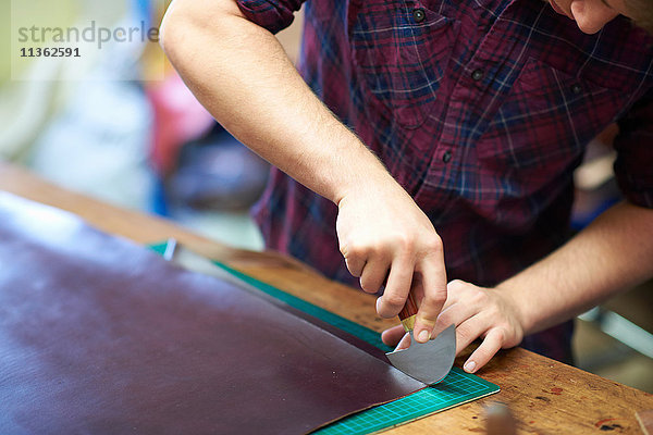 Männlicher Arbeiter in einer Lederwerkstatt  schneidet Leder mit einem Schneidewerkzeug  mittlerer Abschnitt