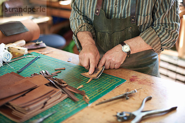 Männlicher Arbeiter in Lederwerkstatt  Überprüfung der Schärfe des Messers auf Leder  Mittelteil