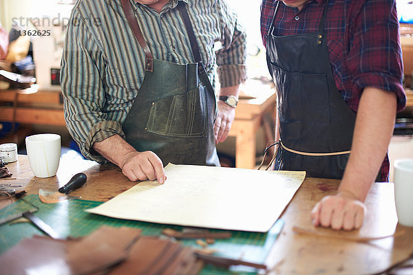 Zwei männliche Arbeiter in der Lederwerkstatt  Blick auf die Pläne  mittlerer Abschnitt