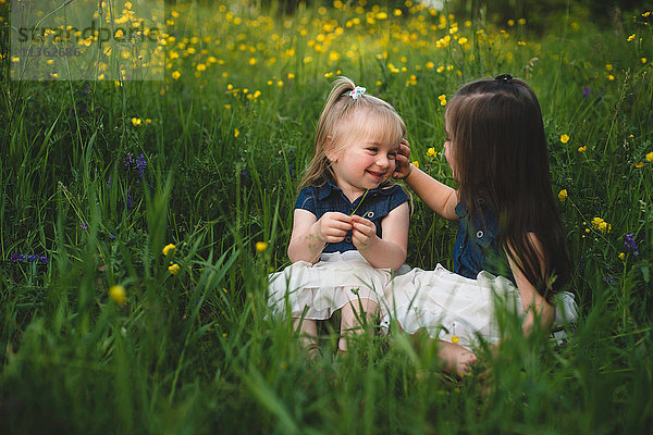 Mädchen sitzen auf einer Wildblumenwiese und lächeln von Angesicht zu Angesicht