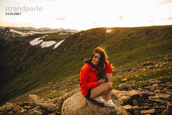 Frau sitzt auf einem Felsen und schaut lächelnd in die Kamera  Rocky Mountain National Park  Colorado  USA