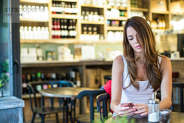 Junge Frau sitzt im Café und liest Smartphone-Texte