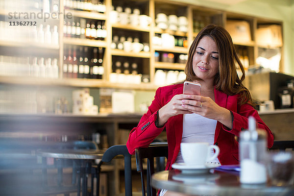 Junge Frau sitzt im Café und liest Smartphone-Update