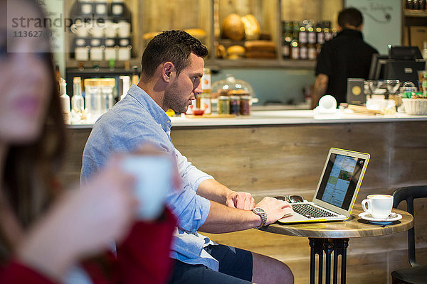 Mann sitzt im Café und liest Laptop