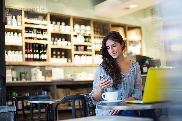 Junge Frau liest Smartphone-Texte im Cafe