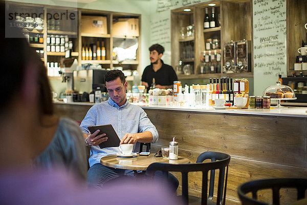 Mann sitzt im Café und blättert am digitalen Tablet