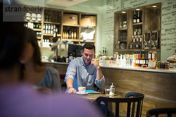 Mann sitzt im Café und redet über Smartphone