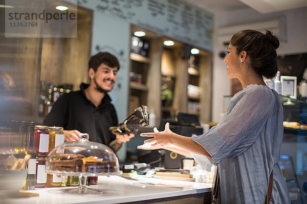 Barista übergibt Baguette an weibliche Kundin an der Café-Theke