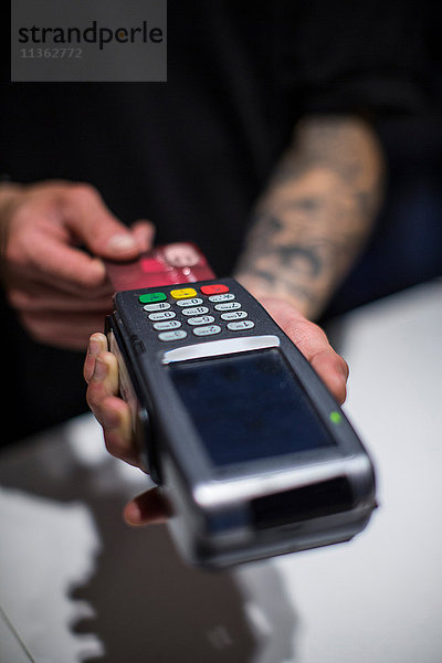 Nahaufnahme der Hände eines jungen Mannes am Kreditkartenautomaten