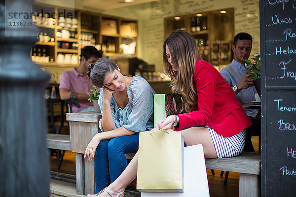 Zwei junge Freundinnen mit Einkaufstaschen unterhalten sich vor dem Café