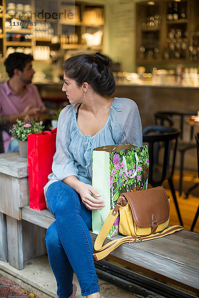 Junge Käuferin sitzt vor einem Café und schaut ihr über die Schulter