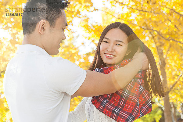 Junger Mann wickelt Tartan-Schal um seine Freundin im Herbstpark  Peking  China