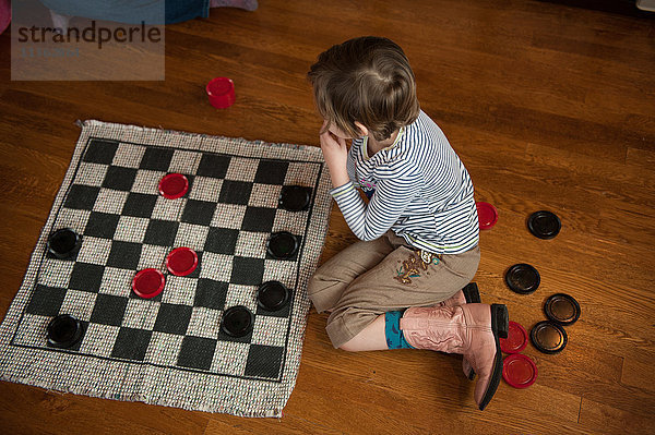 Mädchen sitzt auf Holzboden und spielt Damespiel