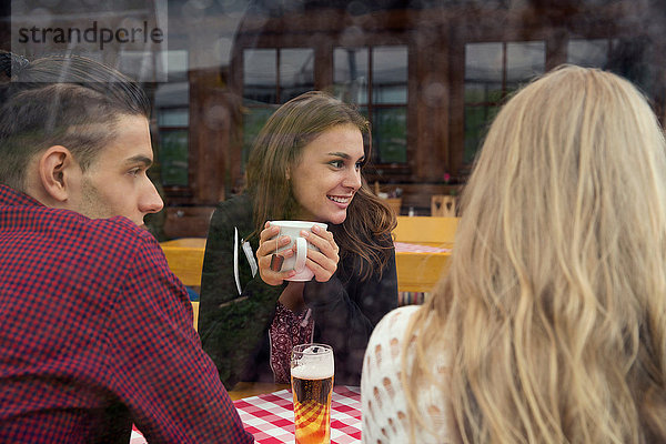 Drei junge erwachsene Freunde mit Kräutertee und Bier im Cafe
