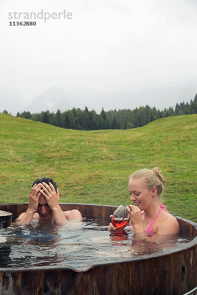 Junges Paar entspannt sich im ländlichen Whirlpool mit Rosenwein  Sattelbergalm  Tirol  Österreich
