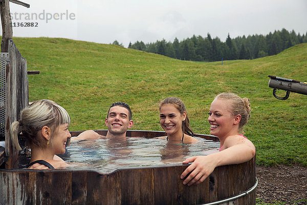 Vier erwachsene Freunde lachen beim Entspannen im ländlichen Whirlpool  Sattelbergalm  Tirol  Österreich
