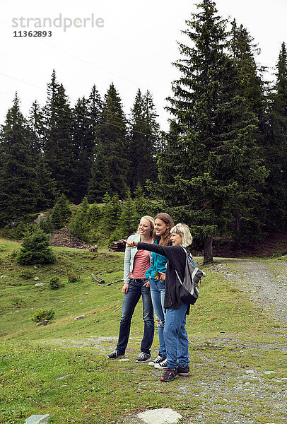 Drei Freundinnen zeigen vom Waldweg aus  Sattelbergalm  Tirol  Österreich