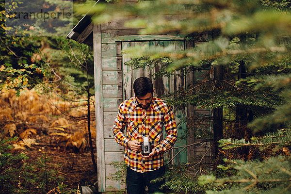 Junger Mann in der Nähe der Hütte im Wald  fotografiert mit Kamera  in der Nähe von Shaver Lake  Kalifornien  USA