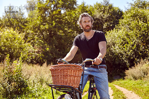 Mittelgroßer erwachsener Mann auf dem Fahrrad  der vom ländlichen Feldweg starrt