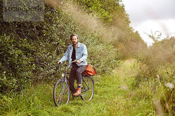 Porträt eines mittelgroßen erwachsenen Mannes auf dem Fahrrad auf einem Feldweg