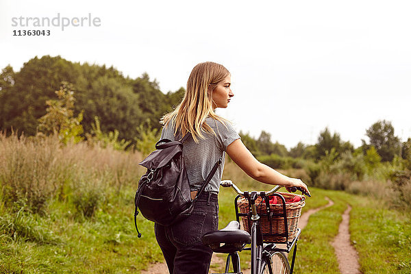 Junge Frau mit Fahrrad  die vom ländlichen Feldweg aus über ihre Schulter schaut