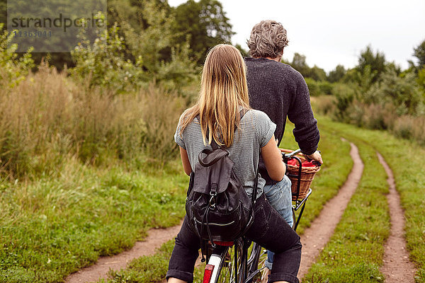 Rückansicht eines Fahrrad fahrenden Paares auf ländlichem Feldweg