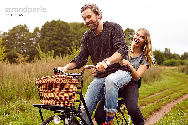 Porträt eines lachenden Paares beim Fahrradfahren auf ländlichem Feldweg