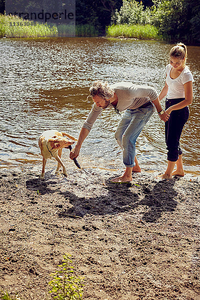 Pärchen spielt mit Hund am Flussufer
