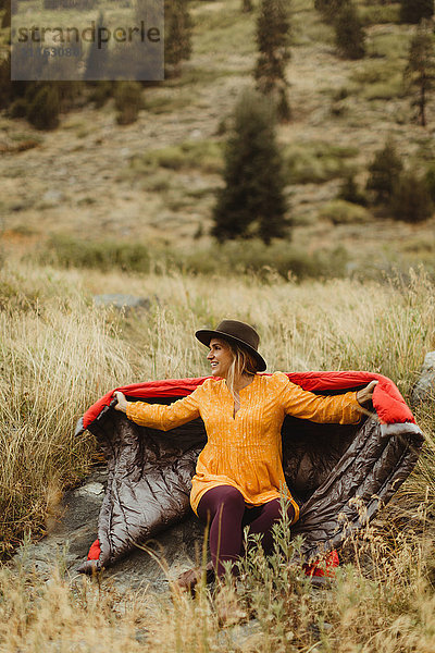 Frau sitzt in ländlicher Umgebung  in einen Schlafsack gehüllt  Mineral King  Sequoia National Park  Kalifornien  USA