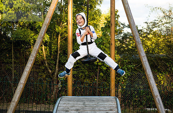 Porträt eines Jungen in Astronautenkostüm  der auf einer Seilrutsche auf dem Spielplatz reitet