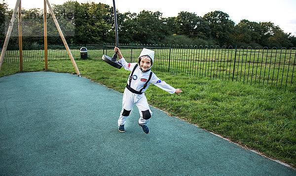Porträt eines Jungen im Astronautenkostüm  der am Seilzug auf dem Spielplatz zieht