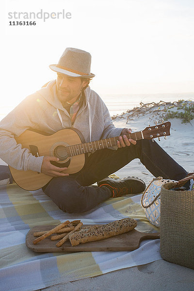 Junger Mann spielt Gitarre auf einer Picknickdecke am Strand  Kapstadt  Westkap  Südafrika